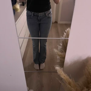 Grå bootcut jeans med broderade fickor - Säljer ett par blå jeans med bootcut-modell och snygga broderade detaljer på bakfickorna. Jeansen har klassisk femficksdesign, normal passform och är tillverkade i jeansmaterial. Perfekta för dig som gillar en avslappnad men ändå stilren look.