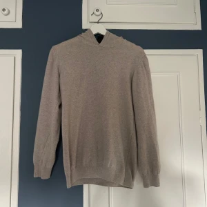 Beige hoodie i kashmir/ull från Oscar Jacobson - Mjuk och lyxig beige hoodie från Oscar Jacobson i kashmir/ull. Tröjan har huva, ribbade muddar och lång ärm. Perfekt för dig som vill ha en stilren och bekväm look med premiumkänsla. Nypris 1500 kr. Aldrig använd. Passar mer som en XS.