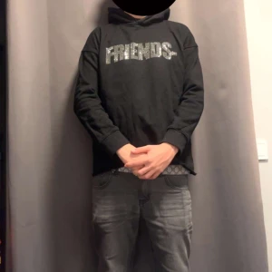 Svart hoodie FRIENDS med strassdetaljer - Svart hoodie från VLONE med glittrande FRIENDS-tryck i strass på bröstet och ett stort V i strass på ryggen. Klassisk huva och långärmad modell, perfekt för dig som gillar streetwear och vill sticka ut med coola detaljer.