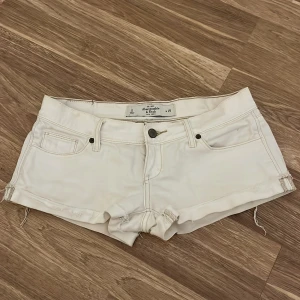 Vita jeansshorts Abercrombie & Fitch - Snygga vita jeansshorts från Abercrombie & Fitch med klassisk femficksdesign, råa kanter och diskreta sömmar på bakfickorna. Modellen är lågmidjad och har stretchigt material för extra komfort. Perfekta till sommaren!