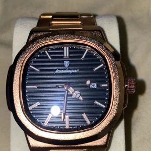 Roséguld Poedagar herrklocka - Snygg herrklocka från Poedagar i roséguld med metallarmband och svart urtavla. Urtavlan har horisontella ränder, datumvisning och minimalistiska indexmarkeringar. Klockan har en fyrkantig form med rundade hörn och en robust känsla. Perfekt för dig som gillar stilrena accessoarer. 
