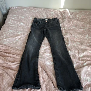 Svarta jeansbyxor från Gina Tricot - Snygga svarta jeansbyxor från Gina Tricot med coola detaljer på bakfickan och slitningar för en trendig look. Klassisk femficksmodell med knapp och dragkedja framtill. Perfekta för dig som gillar en avslappnad men stilren stil.
