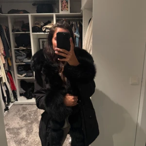 Svart parkajacka med päls - Säljer en svart parkajacka med stora fluffiga detaljer i riktig päls krage, ärmslut och framkant. Jackan har en klassisk parkamodell med lång ärm och snygg oversized känsla. Kan dras in i midjan, storlek S