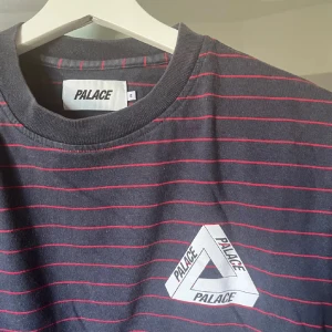 t-shirt från Palace - Svart t-shirt från Palace med tunna röda ränder och klassisk Tri-Ferg-logga tryckt på bröstet. Rund hals och korta ärmar. Skön bomullskvalitet och regular fit, perfekt för dig som gillar streetwear och vill sticka ut med en snygg detalj. Hej jag säljer en lite äldre palace t-shirt som köptes på Herr Judit hornsgatan. Tröjan är i bra skick och har varit sparsamt använd, nypris 1500. Skriv för fler bilder & frågor.