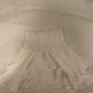 Vit volangkjol - Supersöt vit kortkjol med dubbla volanger. Kjolen är gjord i ett lätt och luftigt tyg, perfekt för varma dagar. 