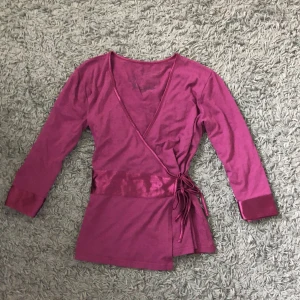 Vinröd omlottopp - Snygg vinröd omlottopp med trevartsärmar. Toppen har v-ringning och knytband i sidan för en justerbar passform. Så fin till exempel till ett par jeans med ett linne under🥰