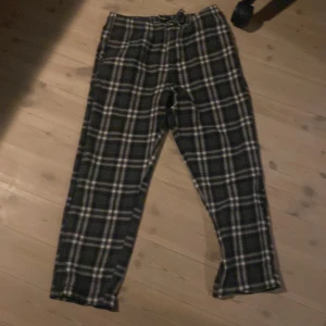 Svarta rutiga byxor med snörning - Snygga svarta byxor med vitt och grått rutmönster och snörning i midjan. Perfekta för en chill och avslappnad stil. Mjukt material som känns skönt mot huden och passar till många olika outfits.