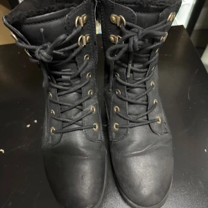 Svarta kängor med snörning, So All - Svarta kängor från So All i storlek 39, tillverkade i skinn med grov gummisula. De har snörning med metallöglor i guldton och mjukt, fluffigt foder på insidan för extra värme. Perfekta för kalla dagar och har en klassisk rund tå och platt sula.