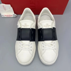 Valentino Garavani Open sneakers vit/svart - Snygga Valentino Garavani Open sneakers i vitt skinn med bred svart läderdetalj över mitten. Klassisk rund tå, vita snören och platt sula. Bak på hälen finns coola vita nitar som ger extra edge. Perfekt för dig som gillar stilrena och lyxiga sneakers.