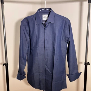 Blå skjorta från The Seven Seas - Snygg blå skjorta från The Seven Seas med klassisk krage och knappar framtill. Skjortan har lång ärm och ett diskret mönster som ger en cool touch. Perfekt för dig som gillar stilrena plagg med lite edge. Storlek L slim fit.