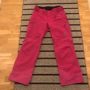 Rosa täckbyxor från Norrøna - Snygga rosa täckbyxor från Norrøna med flera dragkedjeförsedda fickor och justerbar midja. Byxorna har en rak passform och är perfekta för skidåkning eller andra vinteraktiviteter. Materialet är slitstarkt och vattenavvisande, med coola detaljer och broderad logga på benet. Använda endast en gång, säljer pga storlek är för liten. Priser går att diskutera! 