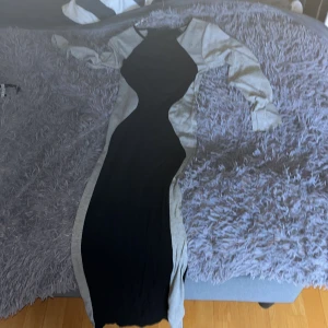 Svart och grå långklänning Club L - Säljer en långklänning från Club L i storlek M. Klänningen är svart med gråa sidor och långa ärmar, vilket ger en snygg kontrast och markerar midjan. Den har en figurnära passform och är tillverkad i ett stretchigt material som sitter bekvämt. Ganska väl använd men är i bra skick