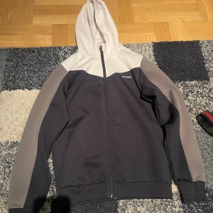 Svart, vitt och grå hoodie från McKenzie - Snygg hoodie från McKenzie i svart, grått och vitt. Tröjan har hel dragkedja framtill, huva i vitt och kontrastfärgade ärmar i grått. Perfekt för när du vill ha en sportig look. Materialet är mjukt och känns skönt mot huden. Den här tröjan är i bra skick och är endast använd några gånger. Enda saken är att den har fått som ett litet skrap märke som du ser på 4 bilden. Jag är kunnig att gå ned i pris lite vid en snabb affär 