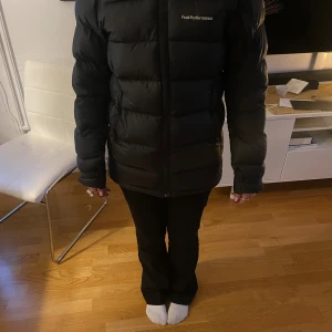 Svart dunjacka Peak Performance XS - Säljer en svart dunjacka från Peak Performance i storlek XS. Jackan har huva, dragkedja framtill och klassisk pufferstil med breda kanaler. Perfekt för kalla dagar och riktigt snygg till streetwear-looken. En dragkedja på fickorna är dock trasig därför priset.