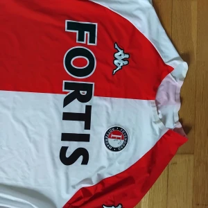 Feyenoord långärmad fotbollströja XL - Säljer en klassisk Feyenoord kortärman slimfitmodell fotbollströja från Kappa i storlek XL. Är som en Litemmn L Tröjan har röd och vit färgblock-design med klubbmärke och sponsortryck på bröstet. Materialet är lätt och andas, perfekt för match eller träning. Kappa-loggor på ärmar och bröst.