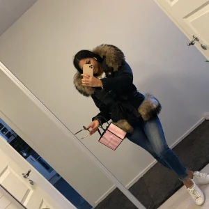 Svart amoress med pälsdetaljer - Kan gå ner i pris vid snabb affär, Säljer en svart parkajacka med stor fluffig päls runt huvan och nederkanten. Jackan har bälte i midjan, knappar och dragkedja framtill. Den är långärmad och har en snygg, lite oversized look. Perfekt för dig som vill ha en varm och stilren jacka med extra attityd. Har även köpt till en stor päls nypris 18 tusen