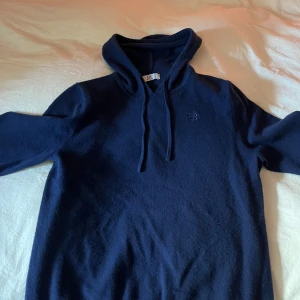 Marinblå hoodie i merinoull & kashmir - Mysig marinblå hoodie från Bvaldi i en lyxig mix av 90% merinoull och 10% kashmir. Tröjan har huva med snörning och broderad logga på bröstet. Perfekt för dig som vill ha en stilren och skön look under kyliga dagar. Inga tecken på användning. Kvitto finns köpt i somras 