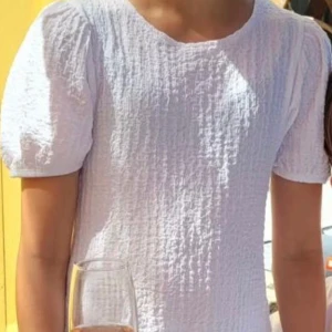 Vit kort klänning med puffärm - Superfin vit kort klänning från Lager 157 med puffärmar och rund hals. Klänningen har en strukturerad, krinklad yta och är lätt utsvängd nertill. Perfekt för sommarens alla tillfällen och ger en fräsch look.