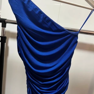 Blå one shoulder topp BikBok XS (pris kan diskuteras)  - Snygg marinblå one shoulder klänning från BikBok i storlek XS. Klänningen har draperad effekt och smala axelband, vilket ger en elegant look. Perfekt för dig som vill sticka ut med en färgstark och modern stil. 