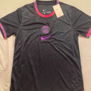 Svart PSG x Nike fotbollströja - Paris Saint-Germain fotbollströja från Nike med lila och rosa detaljer. Tröjan är storlek S, män. Den är helt ny och aldrig använd. Skickar inom 1-3 dagar