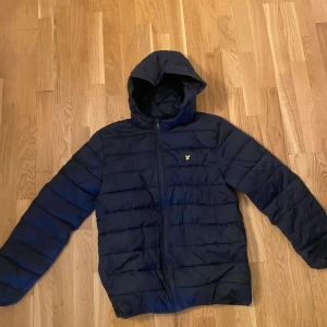 Mörkblå pufferjacka från Lyle & Scott - Snygg mörkblå pufferjacka från Lyle & Scott  med huva och dragkedja framtill. Passar 170-176 enligt beskrivningen. Nypris 1200kr