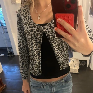 Leopardmönstrad kofta i grått och svart - Säljer en snygg kofta med leopardmönster i grått och svart. Koftan har en knapp framtill, rund halsringning och långa ärmar. Perfekt att slänga över ett linne eller t-shirt för en cool look.🐆