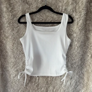 Vit ribbad linnetopp med knytning - Snygg vit ribbad linnetopp med fyrkantig halsringning och  justerbara knytband i sidorna 