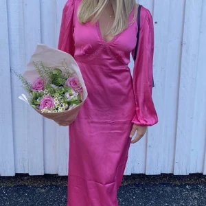 Rosa långklänning i satin med v-ringning - Snygg långklänning med v-ringad hals och långa puffärmar.
