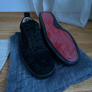 Svarta mockasneakers med röd sula - Säljer ett par svarta sneakers i mocka med snygg snörning och rund tå. Skorna har en unik röd sula med mönster och svart kant runt om. Insidan är ljusbeige och de har en klassisk låg profil som passar till jeans eller dressade outfits. Dom är one of one.