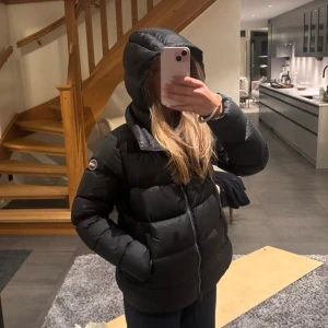 Svart dunjacka från Colmar Originals - Snygg svart dunjacka från Colmar Originals med klassisk puffer-design. Jackan har huva, Perfekt för kalla dagar. Köpt förra vintern men varsamt använd då. Saken som spänner in jackan längst ner är sönder men går kanske att laga. Storlek står ej men passar mig som brukar ha s, 167 lång.  