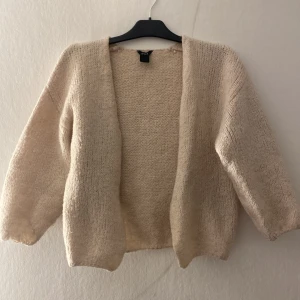 Beige stickad kofta från Lindex - Mysig beige stickad kofta från Lindex i öppen modell. Koftan har långärmade ärmar och en loose passform, perfekt att slänga på sig över en t-shirt eller topp. Enkel och stilren design som funkar till allt.