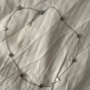 Silverhalsband med stjärnor - Ett tunt halsband i silverfärg från Edblad, dekorerat med små stjärnformade hängen längs hela kedjan. Perfekt för dig som gillar minimalistiska smycken med en twist. Justerbar längd med karbinlås och diskret logga vid låset. Använt endast enstaka gånger❣️ nypris är 449❣️