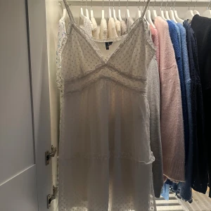 Vit prickig kortklänning Vero Moda - Supersöt vit kortklänning från Vero Moda med tunna axelband, volangdetaljer och diskret prickigt mönster. Klänningen har v-ringning och är tillverkad i ett lätt, luftigt tyg som passar perfekt för varma dagar. En fläck på ryggen (se bild 4), har ej försökt at få bort, men borde gå! Använd 1 gång. 