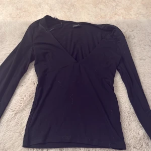 Svart v-ringad topp Gina Tricot XS - Svart långärmad topp från Gina Tricot i storlek XS. Modellen har en djup v-ringning och är figurnära med mjukt stretchigt material, perfekt för att styla med jeans eller kjol. Enkel och stilren design som funkar året runt.