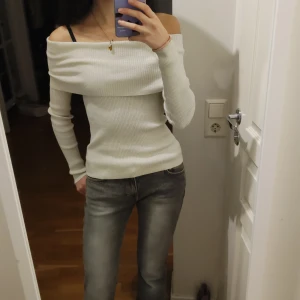 Vit glittrig offshoulder ribbad topp - Säljer en snygg vit offshoulder topp med ribbad struktur. Toppen har lång ärm och sitter tight mot kroppen, perfekt för dig som gillar en stilren och modern look. Materialet är mjukt och stretchigt, vilket gör den bekväm att bära hela dagen.