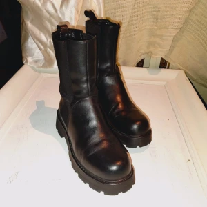 Svarta boots från Vagabond i skinn - Säljer ett par svarta boots från Vagabond i äkta skinn med chunky sula och elastiska paneler på sidorna. Klassisk rund tå och dragflik baktill för enkel påtagning. Perfekta för dig som gillar en stilren och edgy look.