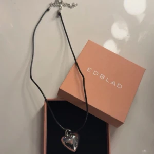 Halsband med hjärta  - Snyggt halsband med ett silverfärgat hjärta som hänge. Kedjan är svart och tunn, vilket ger en stilren kontrast till det blanka hjärtat. Perfekt accessoar för att lyfta din outfit med en personlig touch.