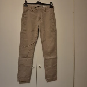 Beiga chinos från NN07, modell Theo - Säljer ett par stilrena beiga chinos från NN07, modell Theo. Byxorna har klassisk rak passform, två fickor fram och två bakfickor med knapp. Tillverkade i 98% bomull och 2% elastan för lite stretch. Perfekta för en clean och avslappnad look.