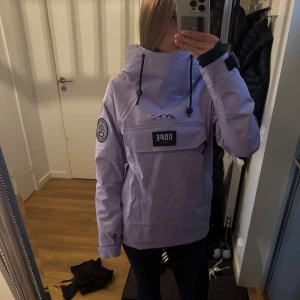 Ljuslila skid- och snowboard jacka från Dope - Säljer en ljuslila vindjacka från Dope med stor magficka, svart logotyp och bergstryck på bröstet. Jackan har huva med snörning, kardborre vid ärmslut och lång ärm. Använd endast 2 gånger. Inga fläckar eller liknande. Skriv för fler frågor och bilder!💕