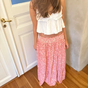 Rosa  långkjol Zara - Säljer en flowy långkjol i rosa med vitt paisleymönster. Kjolen har bred linning och är lätt utställd för en avslappnad vibe. Perfekt för varma dagar och ger en bohemisk känsla. Materialet känns svalt och mjukt mot huden.