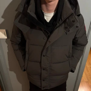 Mörkgrå dunjacka från Canada Goose - Säljer en mörkgrå dunjacka från Canada Goose med klassisk patch på ärmen. Med köp får man päls till luvan samt en Canada goose påse.