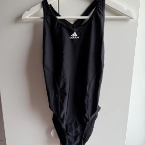 Adidas svart baddräkt, storlek 38 - •Svart baddräkt med Adidas logga framtill och korsade band på ryggen. •Väldigt bra skick. Tvättad såklart.   Djur och rökfritt hem