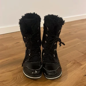 Svarta vinterstövlar med fuskpäls - Svarta vinterstövlar med snörning och fuskpäls upptill. Yttermaterial i syntet och detaljer i skinnimitation. Grov sula med bra grepp och vita kontrastlinjer. Perfekta för kalla dagar när du vill hålla dig varm och torr.lite slitna framtill men är inget särkilt som man tänker på!
