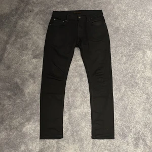 Svarta Nudie Jeans - Svarta jeans från Nudie Jeans i skinny fit med klassisk femficksdesign. Jeansen har smal passform hela vägen ner och är tillverkade i ett stretchigt bomullsmaterial för extra komfort. Perfekta för dig som gillar en stilren look.
