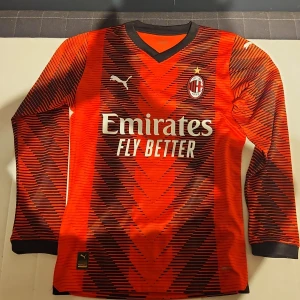 AC Milan långärmad tröja Puma - AC Milan långärmad fotbollströja från Puma i rött och svart med grafiskt mönster. Tröjan har klubbmärke, sponsortryck och svarta muddar. Tillverkad i lätt och ventilerande funktionsmaterial, perfekt för fotbollsplanen. Den är nästan helt nu endast användas 1 gång.
