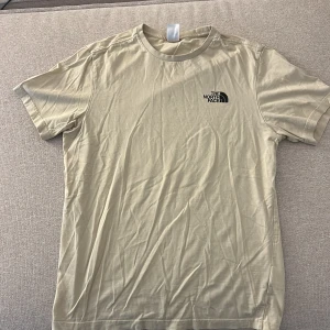 Beige t-shirt från The North Face - Snygg beige t-shirt från The North Face med diskret logga på bröstet. Klassisk rund hals och korta ärmar. Tillverkad i mjuk bomull som känns skön mot huden. Perfekt för dig som gillar stilrena och enkla plagg med en sportig touch.