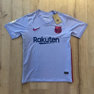 Ljusblå FC Barcelona Nike fotbollströja - Säljer en ljusblå FC Barcelona matchtröja från Nike med Dri-Fit material. Tröjan har korta ärmar, v-ringad krage och tryckta detaljer som Rakuten-logga, klubbmärke och röd Nike swoosh. La Liga-märke på ena ärmen. Perfekt för dig som älskar Barca!