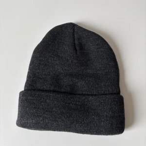 Mörkgrå stickad mössa - En enkel och stilren mörkgrå stickad mössa med uppvikt kant. Perfekt för kalla dagar och passar till de flesta outfits. Mjuk och skön känsla, håller dig varm hela vintern. Helt ny.