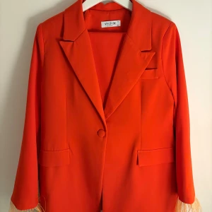 Röd kostym från Mygiyim, stl 42 XL - Snygg orange kostym från Mygiyim i storlek 42/XL. Kavajen har klassisk krage, enkel knappstängning och två fickor framtill. Byxorna är raka och matchar kavajen perfekt. Kostymen är i ett mjukt, lätt material och har en riktigt poppig färg som sticker ut.
