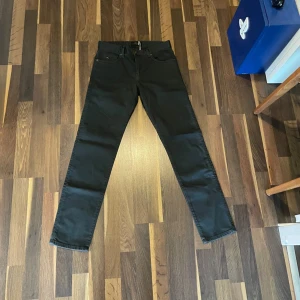 Svarta jeansbyxor från J.Lindeberg - Snygga svarta jeansbyxor från J.Lindeberg med klassisk femficksdesign och raka ben. Perfekta för dig som gillar stilrena och tidlösa plagg. Passar till många olika outfits och är enkla att matcha.